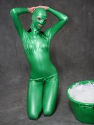 Busty babe in green latex jumpsuit posing with a bowl